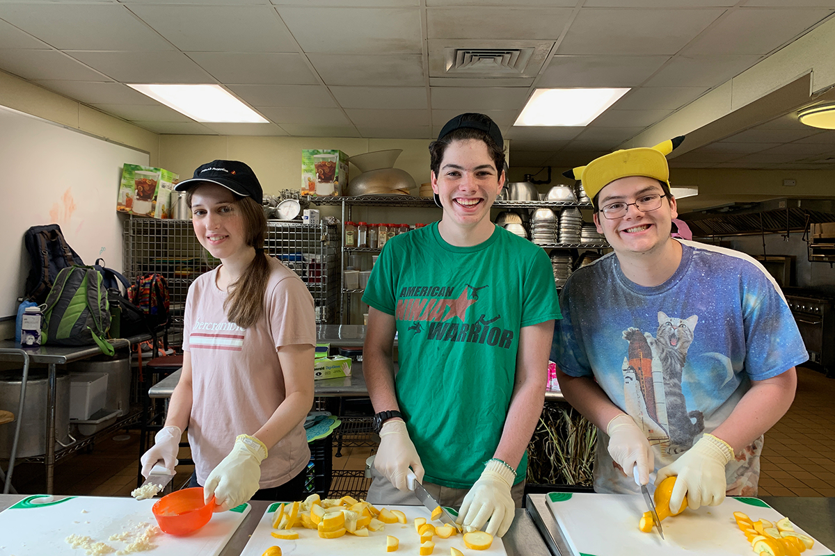 three campers in a kitchen cutting vegetables